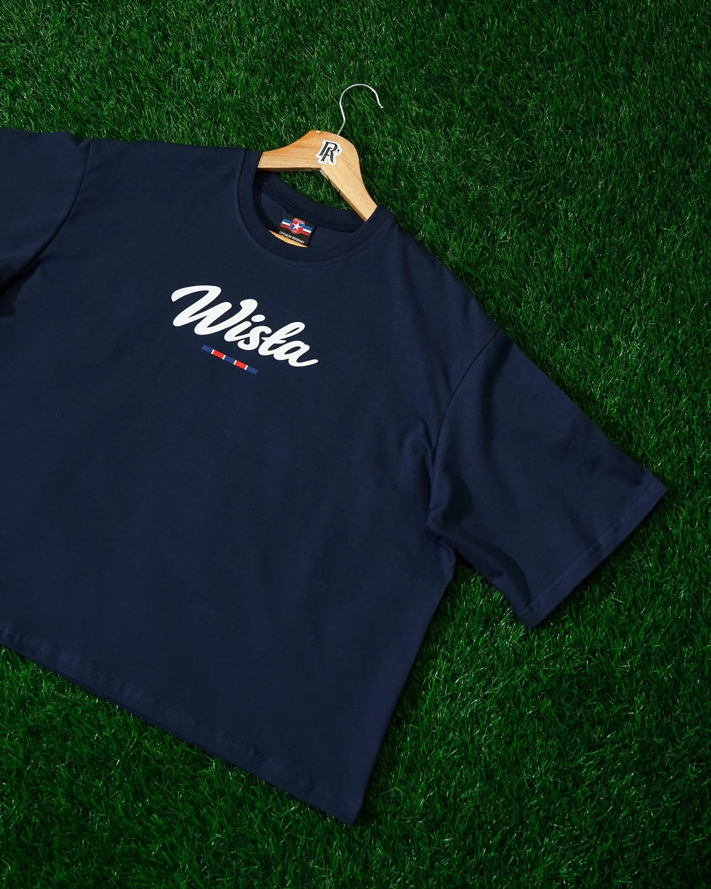Granatowy damski t-shirt oversize na wieszaku, leżący na sztucznej trawie, z białym napisem Wisła na przodzie