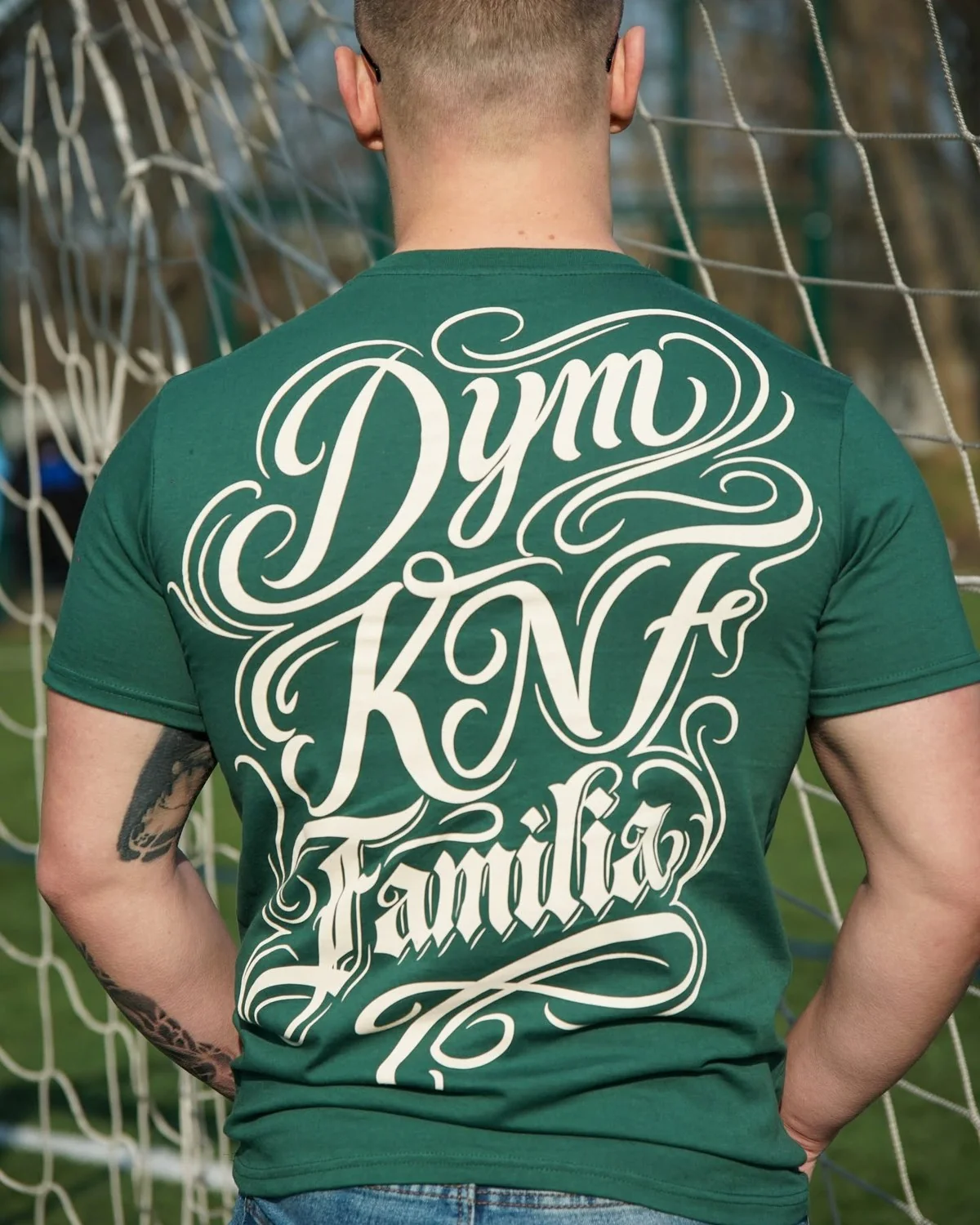 Tył zielonego T-shirtu z dużym białym napisem kaligraficznym